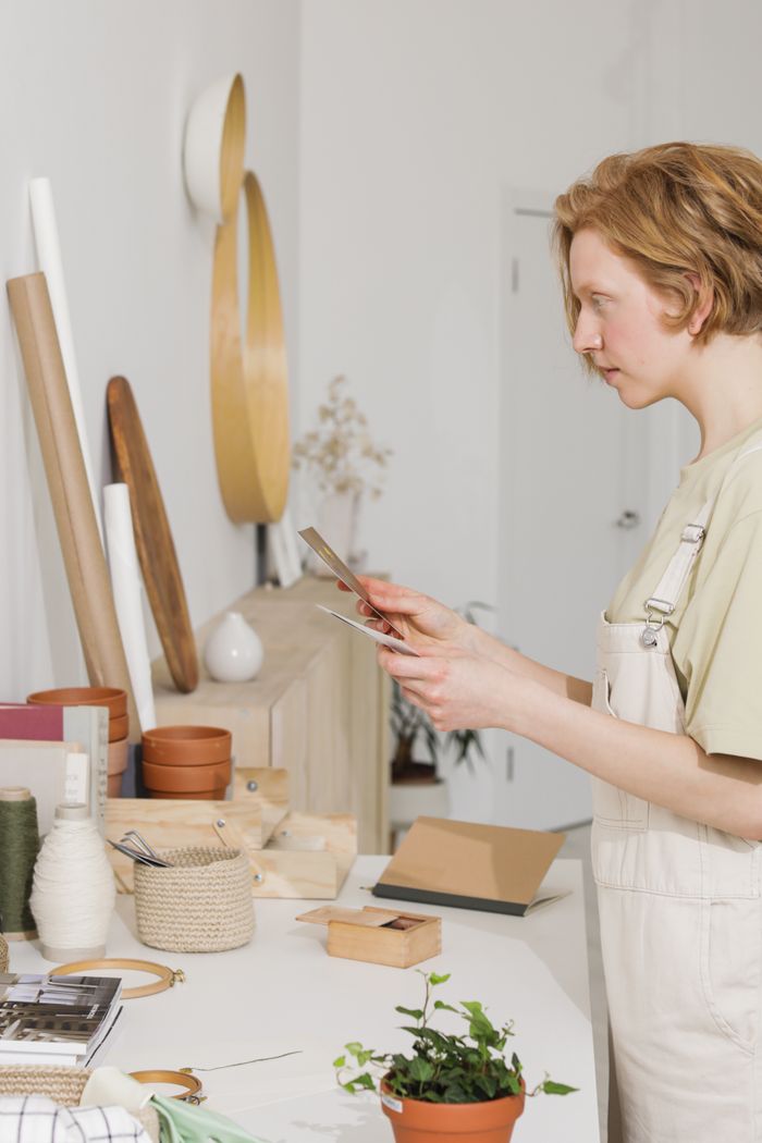 A woman explores home decor designs with craft materials in a minimalist studio setting.