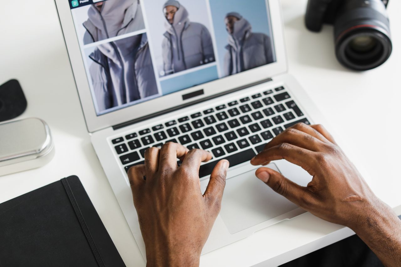 Close-up of hands typing on a laptop displaying a fashion website with a camera nearby.